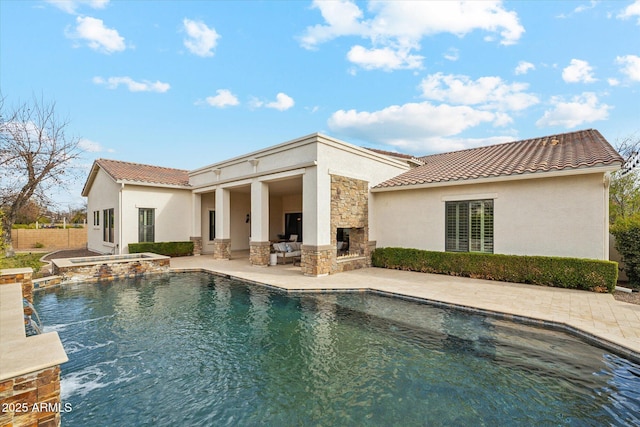 rear view of house featuring fence, a tile roof, stucco siding, an outdoor stone fireplace, and a patio area