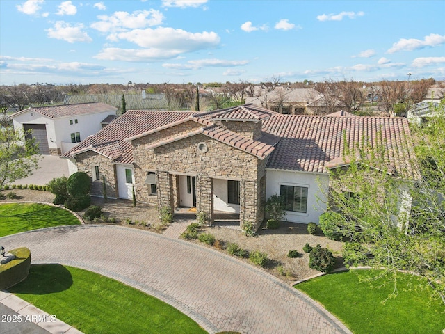 mediterranean / spanish-style house featuring a tiled roof, stone siding, and stucco siding