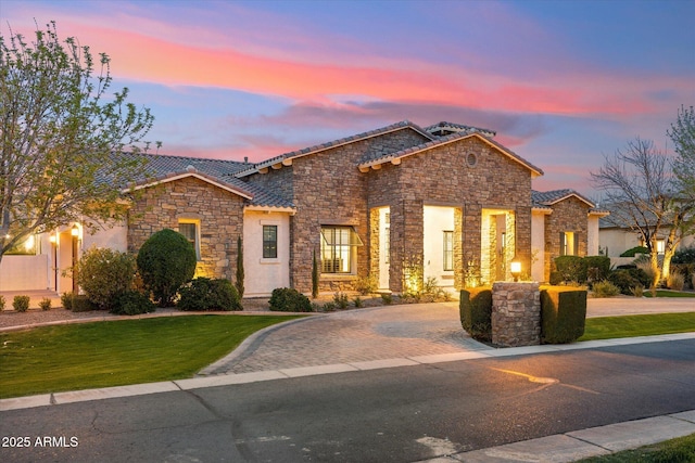 view of front of house featuring stucco siding, a front lawn, stone siding, a tiled roof, and decorative driveway