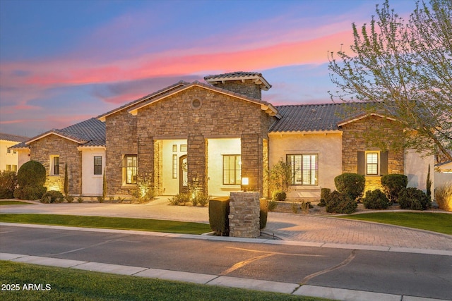 view of front of house featuring stone siding, stucco siding, a tile roof, and a lawn