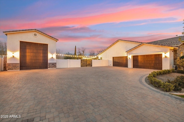 exterior space featuring decorative driveway, fence, stone siding, and stucco siding