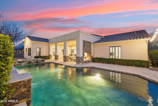 back of house featuring a patio area, stone siding, stucco siding, and a tiled roof