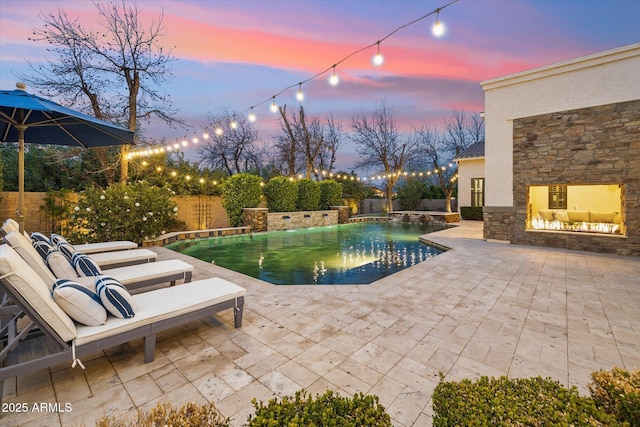 pool at dusk featuring a fenced in pool, a patio, an outdoor stone fireplace, and a fenced backyard