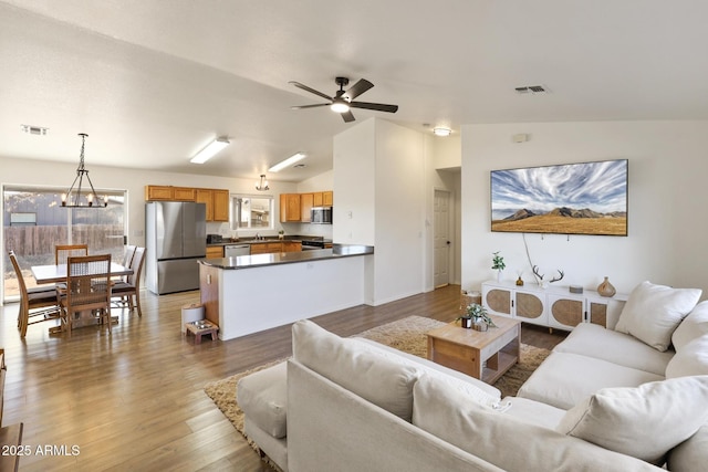 living room with ceiling fan with notable chandelier, visible vents, vaulted ceiling, and wood finished floors