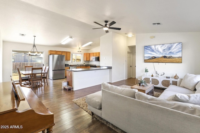 living area with dark wood-style floors, visible vents, vaulted ceiling, and ceiling fan with notable chandelier