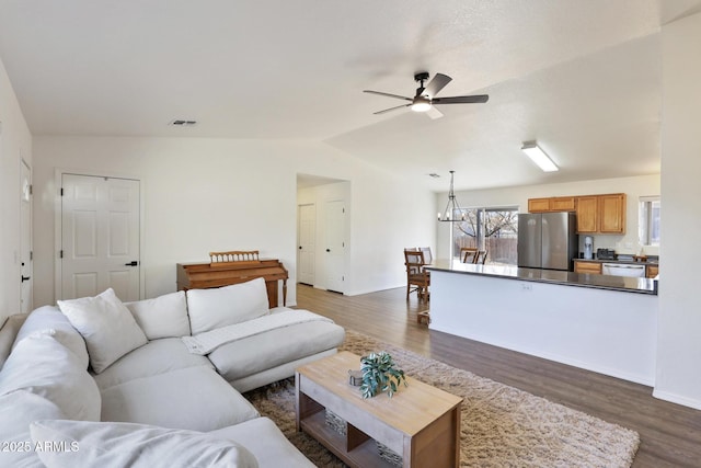 living room featuring dark wood-style floors, baseboards, vaulted ceiling, and ceiling fan with notable chandelier