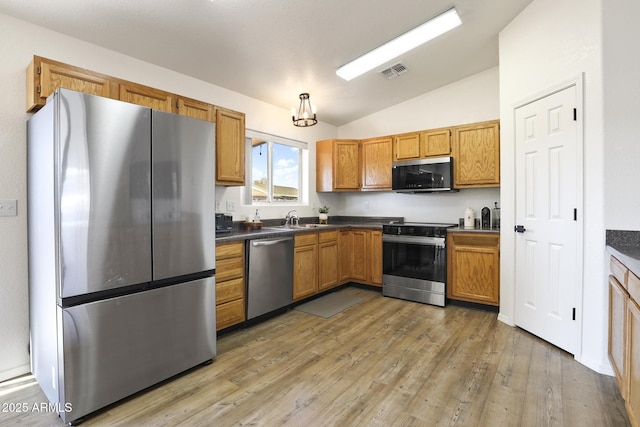 kitchen featuring dark countertops, lofted ceiling, visible vents, appliances with stainless steel finishes, and a sink