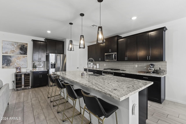 kitchen with sink, an island with sink, stainless steel appliances, and decorative light fixtures