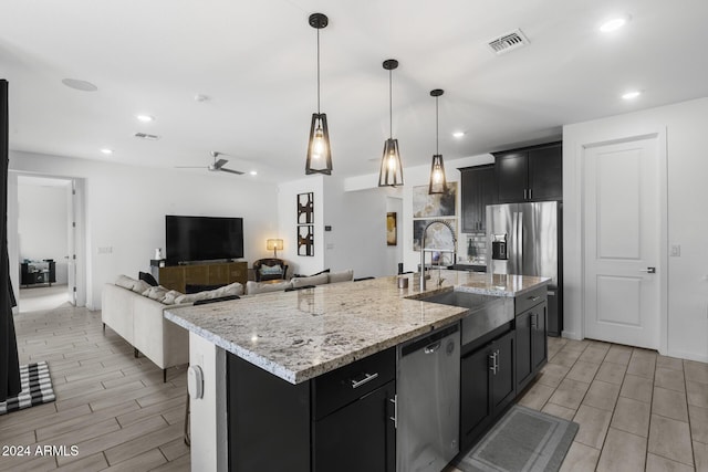 kitchen featuring a center island with sink, ceiling fan, light wood-type flooring, appliances with stainless steel finishes, and decorative light fixtures