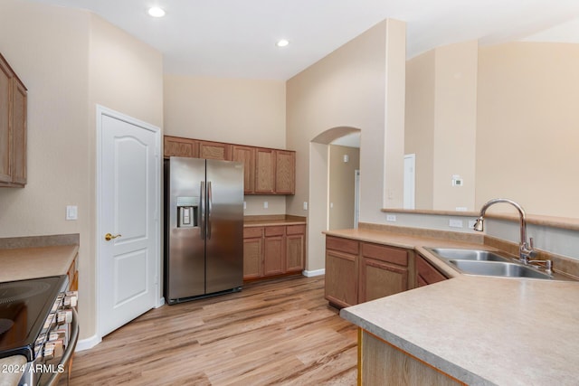 kitchen featuring sink, a towering ceiling, light wood-type flooring, and appliances with stainless steel finishes