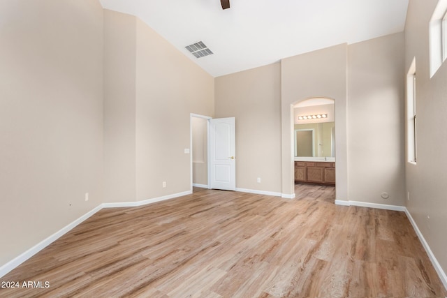 unfurnished bedroom with ceiling fan, light hardwood / wood-style floors, a towering ceiling, and ensuite bath