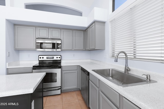 kitchen featuring stainless steel appliances, gray cabinets, light countertops, light tile patterned flooring, and a sink