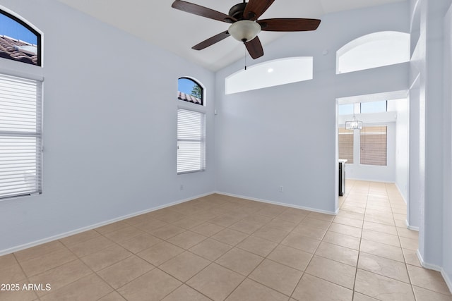 empty room with high vaulted ceiling, light tile patterned flooring, a ceiling fan, and baseboards