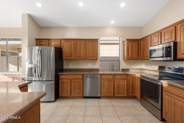 kitchen with appliances with stainless steel finishes, a wealth of natural light, dark stone counters, and sink