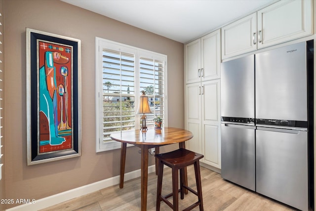 kitchen with light wood-style flooring, white cabinetry, freestanding refrigerator, and baseboards