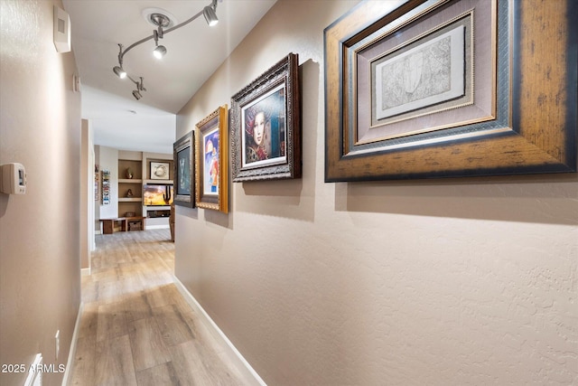 hall with built in features, baseboards, track lighting, and light wood finished floors