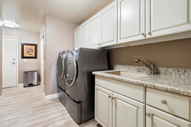 washroom featuring baseboards, light wood finished floors, washing machine and clothes dryer, cabinet space, and a sink