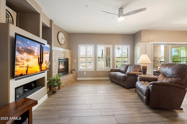 living room with a healthy amount of sunlight, a fireplace, a ceiling fan, and baseboards