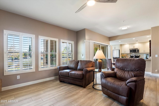 living area featuring baseboards, light wood finished floors, and ceiling fan