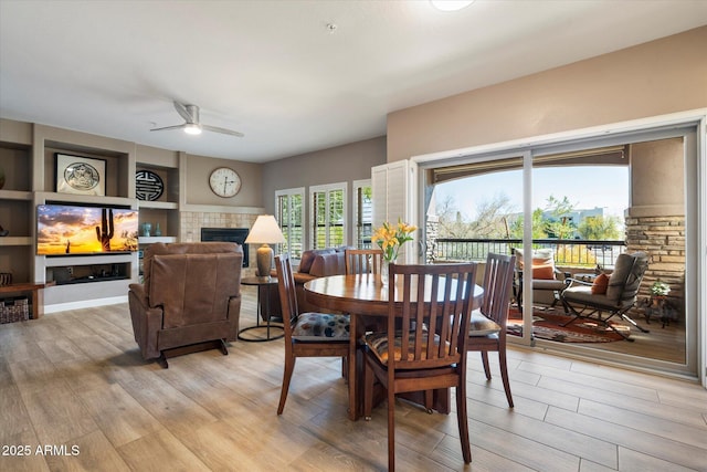 dining room with a ceiling fan, light wood-style flooring, and a fireplace