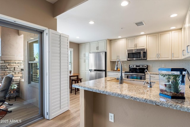 kitchen with light wood finished floors, light stone countertops, decorative backsplash, appliances with stainless steel finishes, and a peninsula