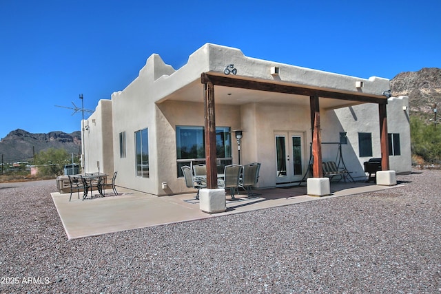 rear view of property featuring a mountain view, stucco siding, french doors, and a patio