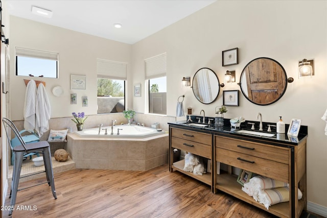 bathroom with double vanity, a garden tub, a sink, and wood finished floors