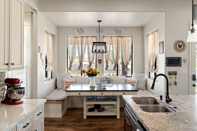 kitchen featuring dark wood-style flooring, a sink, light stone countertops, breakfast area, and pendant lighting