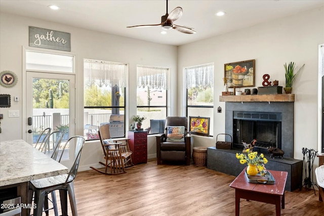 living room featuring a fireplace with raised hearth, wood finished floors, a ceiling fan, and a healthy amount of sunlight