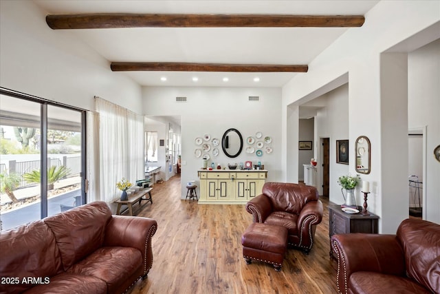 living area featuring beam ceiling, a high ceiling, wood finished floors, and visible vents