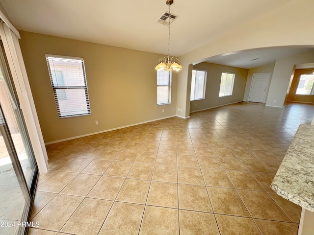 empty room with plenty of natural light, light tile patterned floors, and a chandelier