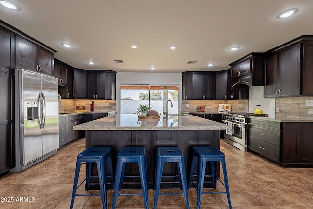 kitchen featuring a center island with sink, light stone counters, and appliances with stainless steel finishes