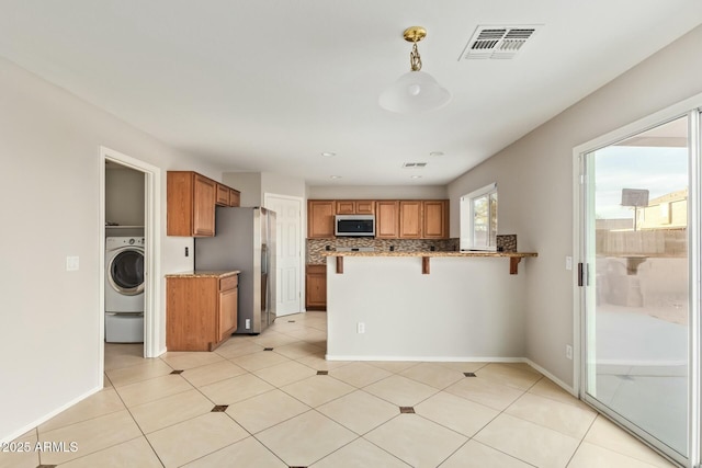 kitchen with appliances with stainless steel finishes, backsplash, a kitchen bar, washer / clothes dryer, and kitchen peninsula