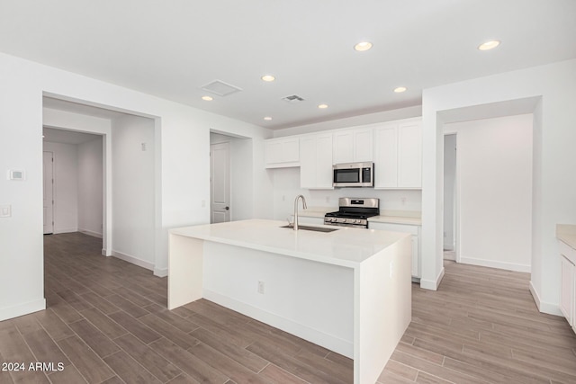 kitchen featuring an island with sink, appliances with stainless steel finishes, light countertops, white cabinetry, and a sink