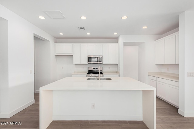 kitchen with stainless steel appliances, white cabinets, and a center island with sink