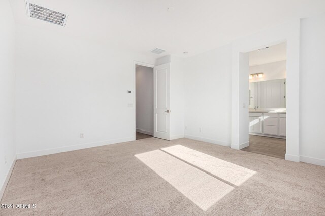 unfurnished bedroom with light carpet, connected bathroom, visible vents, and baseboards