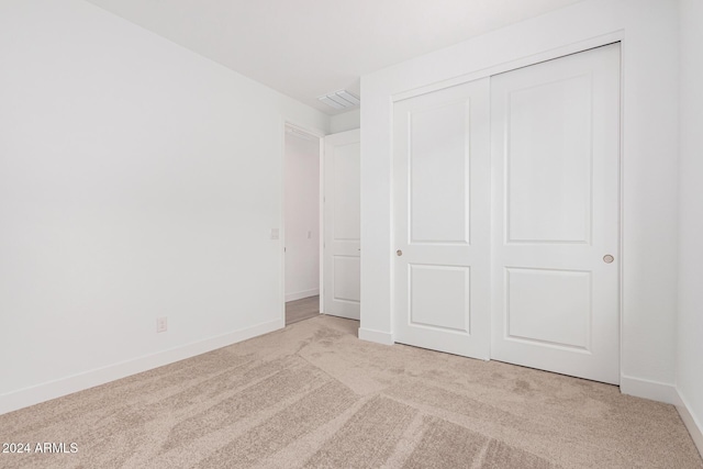 unfurnished bedroom with a closet, light colored carpet, visible vents, and baseboards