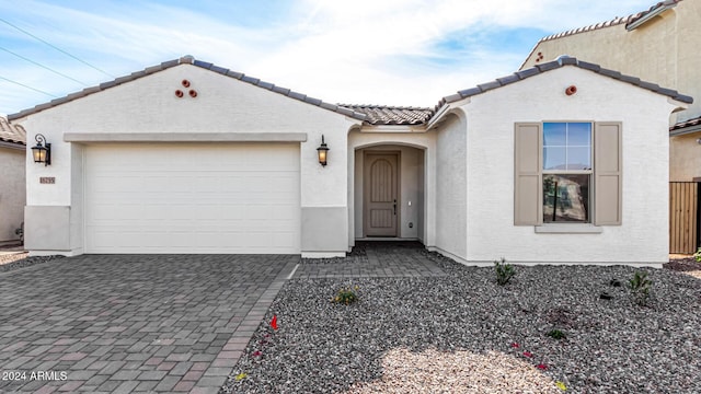 mediterranean / spanish-style house featuring an attached garage, a tile roof, decorative driveway, and stucco siding