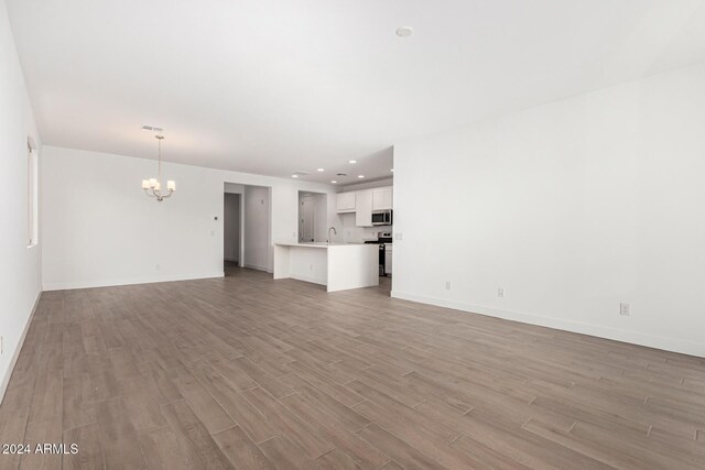 unfurnished living room featuring an inviting chandelier, light wood-style flooring, baseboards, and recessed lighting