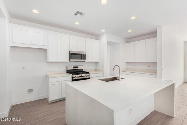 kitchen with stainless steel appliances, light countertops, white cabinetry, a sink, and an island with sink