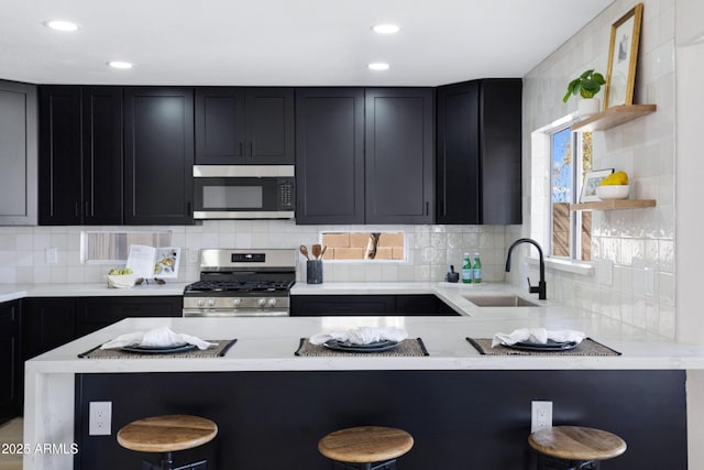 kitchen with stainless steel appliances, a peninsula, a sink, a kitchen breakfast bar, and backsplash