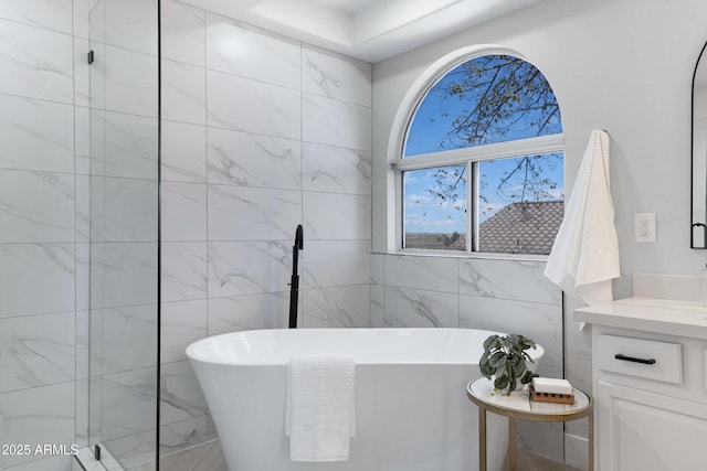 bathroom featuring a freestanding bath, vanity, and tile walls