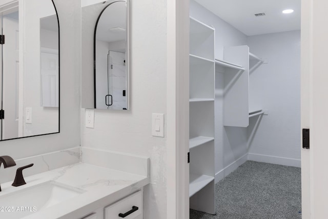 bathroom featuring visible vents, a walk in closet, vanity, and baseboards