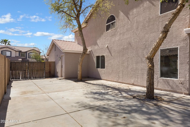 view of property exterior featuring a tiled roof, a gate, fence, a patio area, and stucco siding