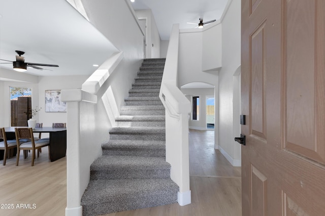 staircase featuring ceiling fan, arched walkways, wood finished floors, and baseboards