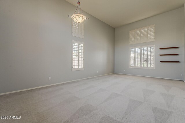 empty room featuring baseboards, a towering ceiling, and light colored carpet