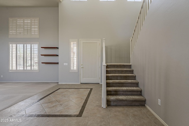 tiled entryway featuring baseboards, a high ceiling, and plenty of natural light
