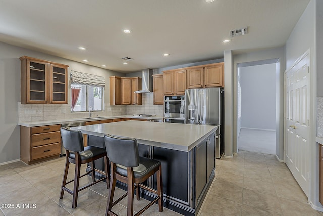 kitchen with visible vents, a kitchen island, appliances with stainless steel finishes, a sink, and wall chimney range hood