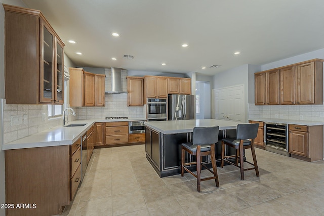 kitchen featuring wall chimney exhaust hood, stainless steel appliances, a sink, beverage cooler, and a center island