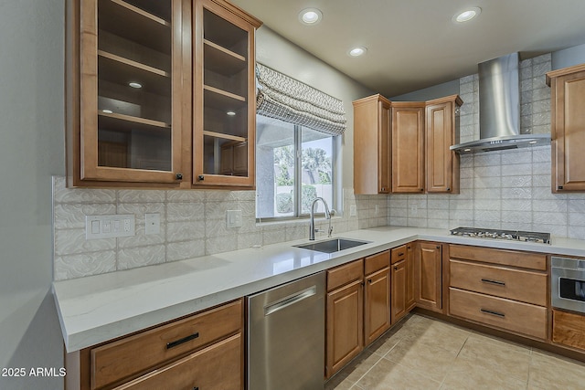kitchen with light countertops, stainless steel appliances, glass insert cabinets, a sink, and wall chimney range hood